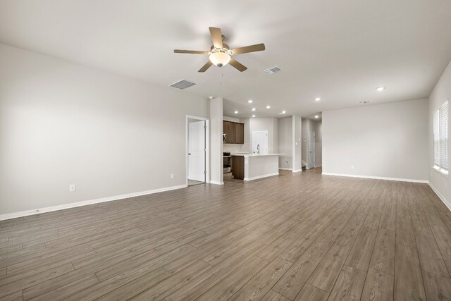 unfurnished living room with ceiling fan, sink, and wood-type flooring