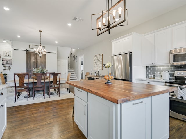 kitchen featuring butcher block counters, hanging light fixtures, a barn door, and appliances with stainless steel finishes