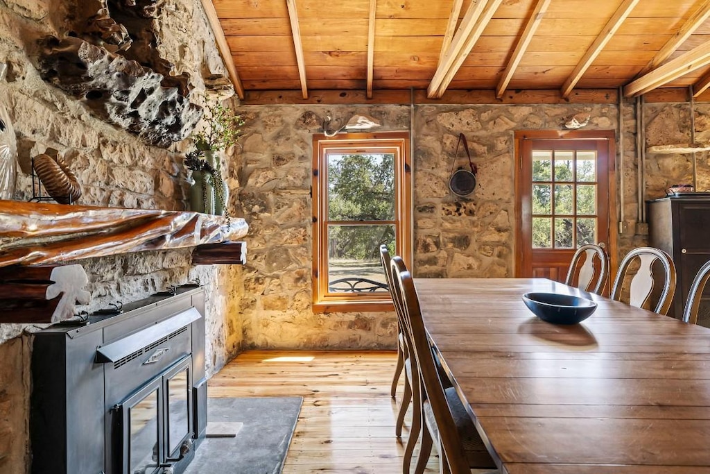 unfurnished dining area with beam ceiling, wood ceiling, a wood stove, and light wood-type flooring