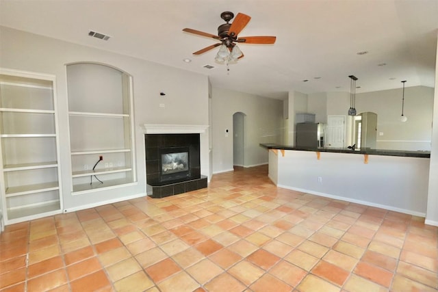 unfurnished living room with built in shelves, ceiling fan, light tile patterned floors, and a tile fireplace