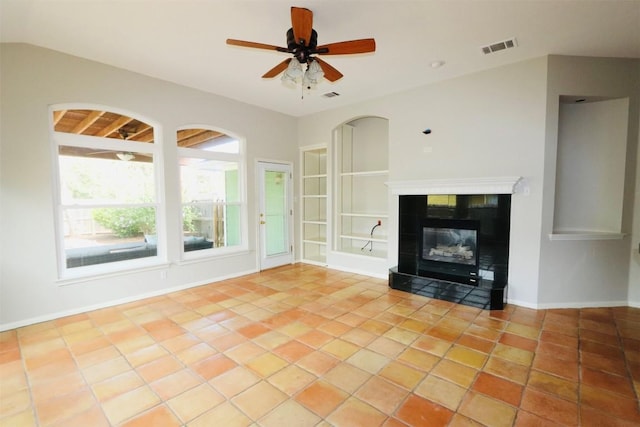 unfurnished living room with built in shelves, ceiling fan, a fireplace, and light tile patterned floors