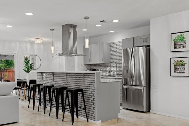 kitchen featuring stainless steel refrigerator with ice dispenser, decorative backsplash, island range hood, sink, and gray cabinetry