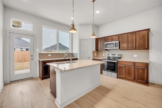 kitchen with sink, hanging light fixtures, stainless steel appliances, light stone countertops, and a center island with sink