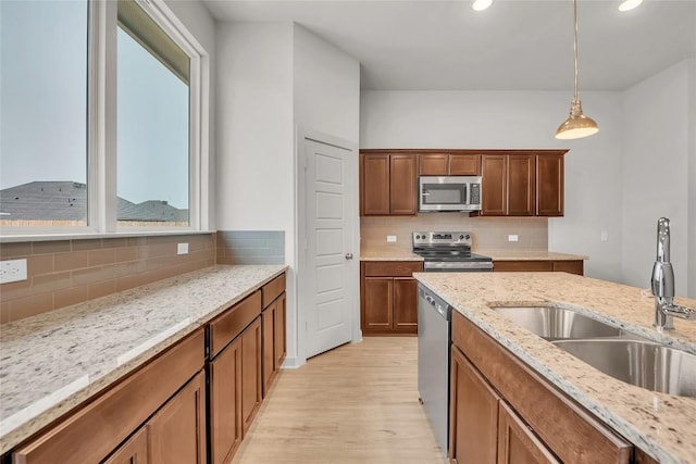 kitchen with sink, hanging light fixtures, stainless steel appliances, light stone countertops, and light hardwood / wood-style floors