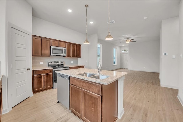 kitchen with sink, a kitchen island with sink, hanging light fixtures, stainless steel appliances, and light stone counters