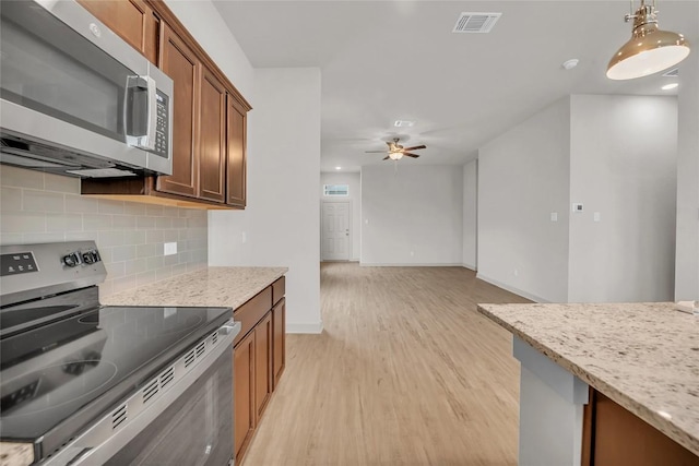 kitchen featuring light stone counters, light wood-type flooring, pendant lighting, stainless steel appliances, and decorative backsplash