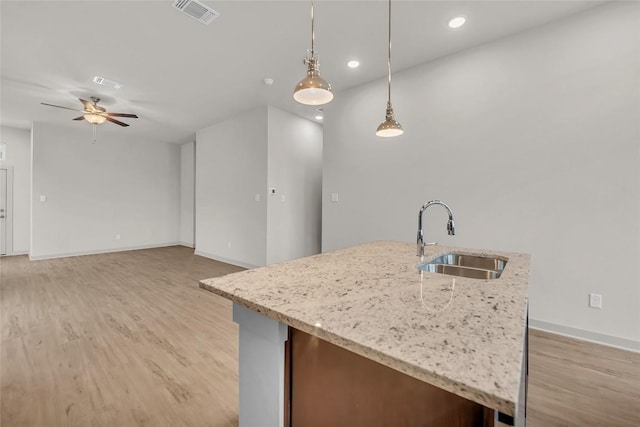 kitchen featuring a center island with sink, sink, pendant lighting, and light wood-type flooring