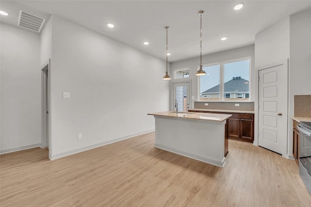 kitchen with sink, light hardwood / wood-style flooring, pendant lighting, a kitchen island with sink, and decorative backsplash