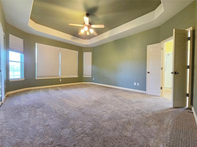 carpeted empty room with ceiling fan and a tray ceiling