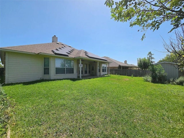 rear view of property with a yard, solar panels, and a storage shed