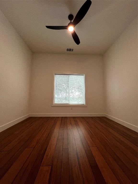 empty room featuring visible vents, ceiling fan, dark wood-style flooring, and baseboards