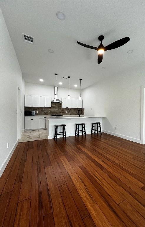 unfurnished living room with light wood finished floors, visible vents, ceiling fan, and baseboards