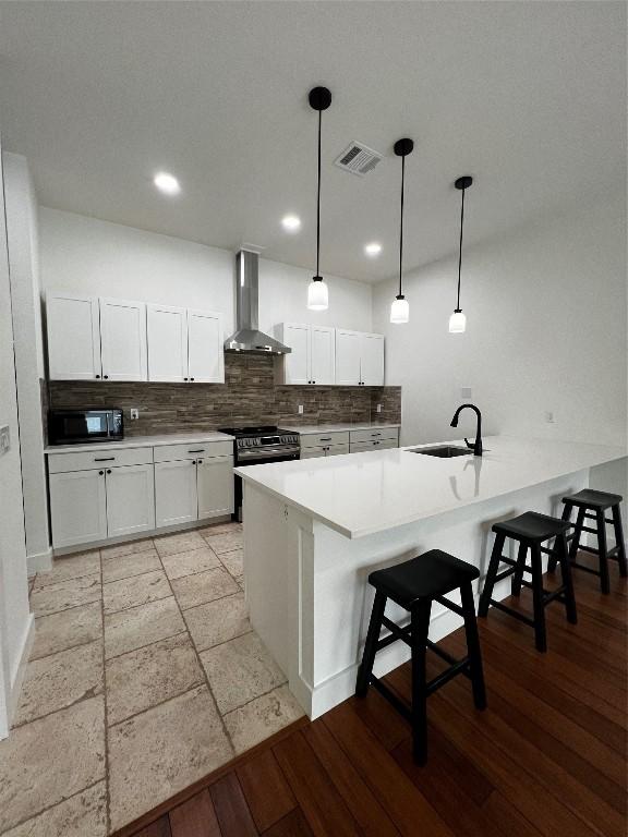 kitchen with stainless steel range, wall chimney range hood, black microwave, a sink, and visible vents