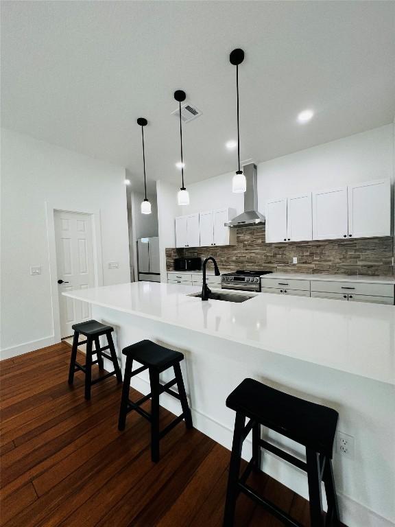 kitchen with a sink, decorative backsplash, a kitchen bar, wall chimney exhaust hood, and appliances with stainless steel finishes