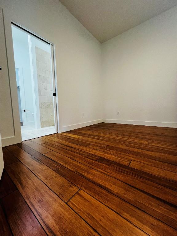 unfurnished room featuring dark wood-style flooring, vaulted ceiling, and baseboards