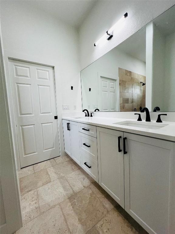 full bathroom with double vanity, stone finish floor, a tile shower, and a sink