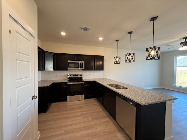 kitchen featuring pendant lighting, appliances with stainless steel finishes, kitchen peninsula, and light stone countertops