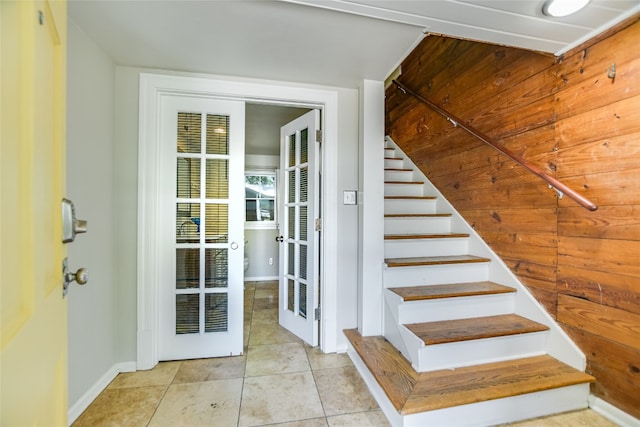 stairway with wooden walls and tile patterned floors