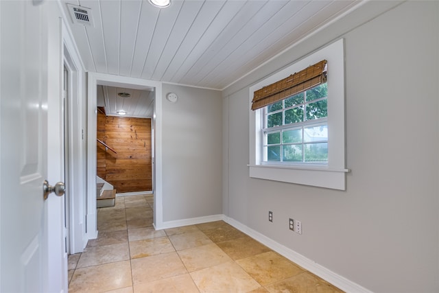 empty room with light tile patterned flooring, wooden walls, and wood ceiling