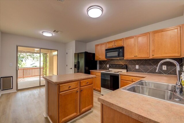 kitchen featuring light wood-type flooring, backsplash, sink, black appliances, and a kitchen island