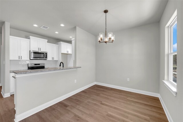 kitchen featuring hanging light fixtures, kitchen peninsula, light hardwood / wood-style flooring, white cabinetry, and appliances with stainless steel finishes