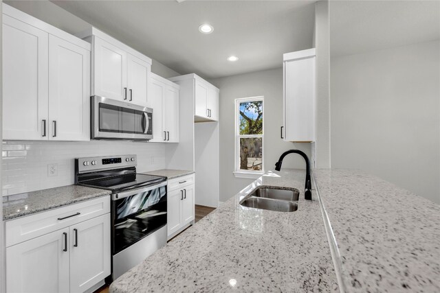 kitchen with stainless steel appliances, white cabinets, light stone counters, and sink