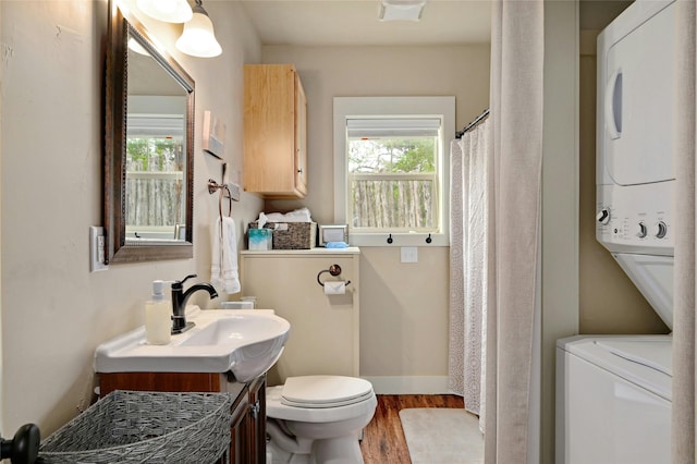 bathroom featuring curtained shower, stacked washer / dryer, vanity, toilet, and hardwood / wood-style flooring