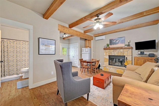 living room with hardwood / wood-style floors, beamed ceiling, a stone fireplace, a wall unit AC, and ceiling fan