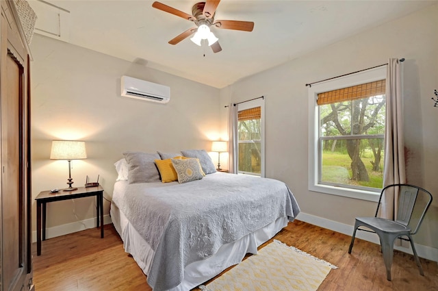 bedroom with ceiling fan, a wall mounted AC, and light hardwood / wood-style floors