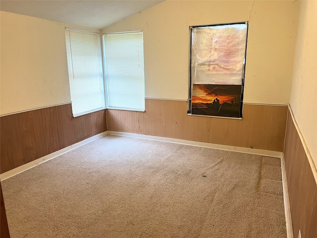 carpeted empty room with wainscoting, lofted ceiling, and wood walls