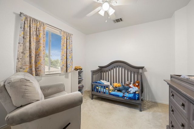 bedroom with light carpet, a crib, and ceiling fan