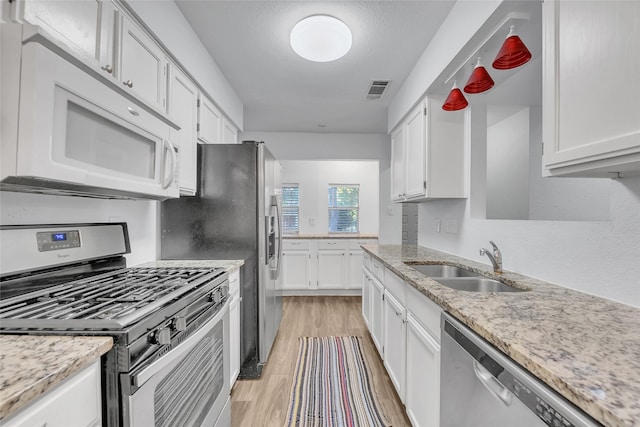 kitchen with stainless steel appliances, white cabinets, light hardwood / wood-style flooring, light stone counters, and sink