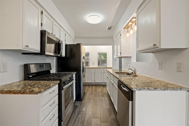 3411 Thomas Kincheon St, Austin, TX 78745 - kitchen with appliances with stainless steel finishes, white cabinets, wood finish floors, light stone counters, and a textured wall