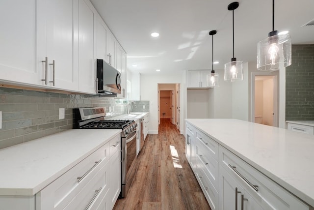 kitchen with white cabinetry, tasteful backsplash, appliances with stainless steel finishes, hardwood / wood-style flooring, and decorative light fixtures