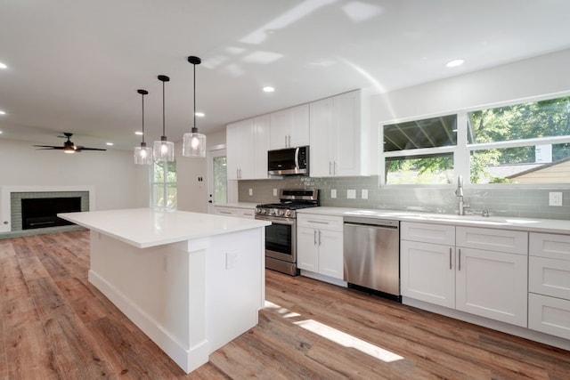 kitchen with appliances with stainless steel finishes, white cabinets, hardwood / wood-style floors, a fireplace, and decorative backsplash