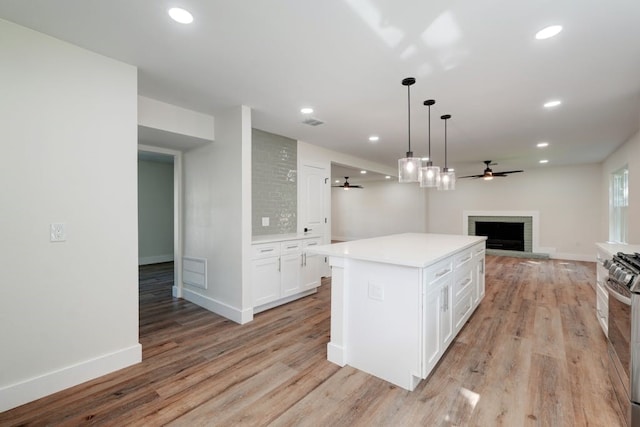 kitchen with a fireplace, ceiling fan, white cabinets, a kitchen island, and light hardwood / wood-style flooring