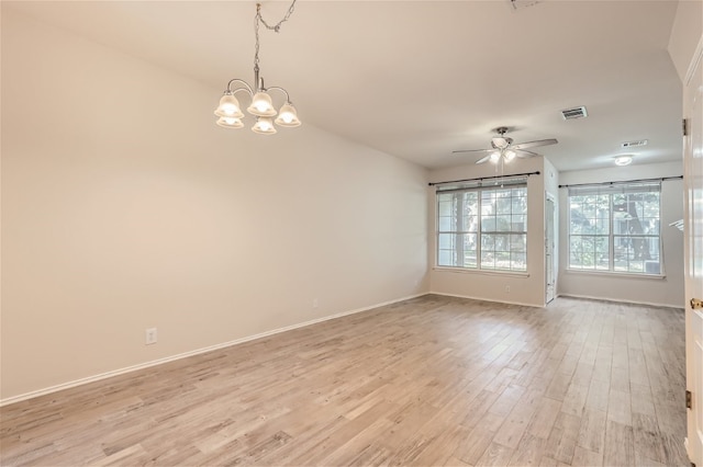empty room featuring baseboards, ceiling fan with notable chandelier, light wood-style flooring, and visible vents