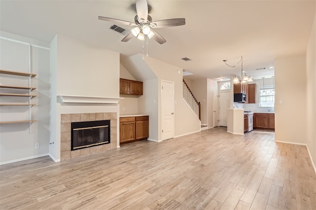 unfurnished living room with a tile fireplace, ceiling fan with notable chandelier, and light hardwood / wood-style floors