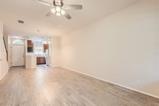 unfurnished living room with baseboards, ceiling fan with notable chandelier, and light wood-type flooring