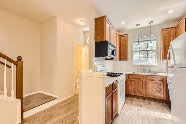 kitchen featuring sink, pendant lighting, white appliances, light hardwood / wood-style floors, and decorative backsplash