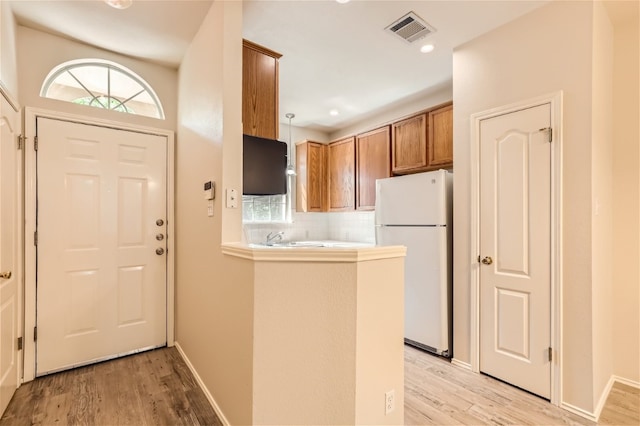 kitchen with decorative light fixtures, decorative backsplash, white refrigerator, kitchen peninsula, and light wood-type flooring