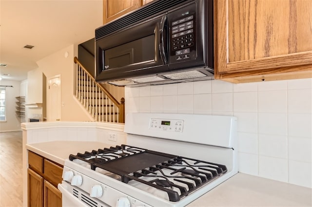 kitchen featuring black microwave, brown cabinetry, backsplash, visible vents, and white range with gas cooktop