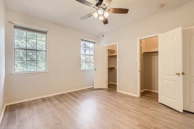 unfurnished bedroom featuring baseboards, a spacious closet, ceiling fan, and light wood-style floors