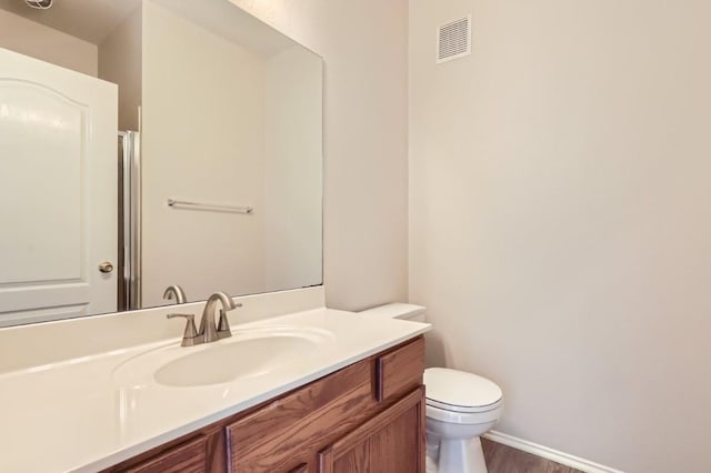 bathroom featuring visible vents, wood finished floors, vanity, baseboards, and toilet