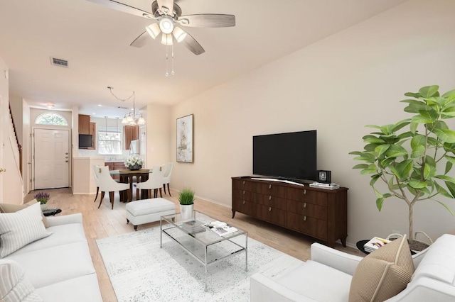 living room with visible vents, light wood-style flooring, ceiling fan with notable chandelier, and baseboards