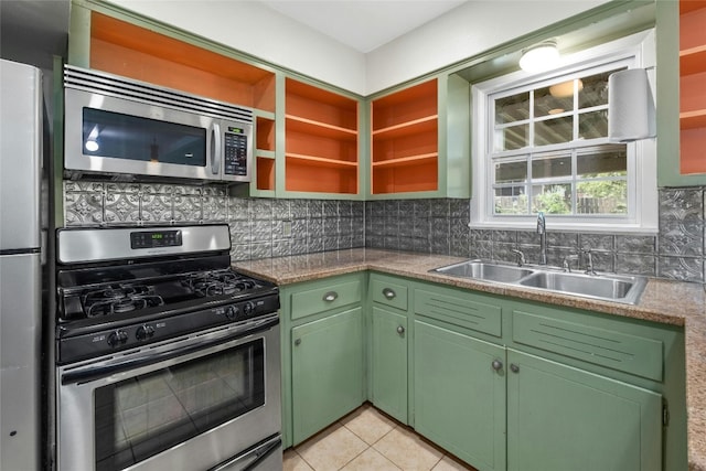 kitchen featuring light tile patterned floors, green cabinetry, a sink, stainless steel appliances, and backsplash