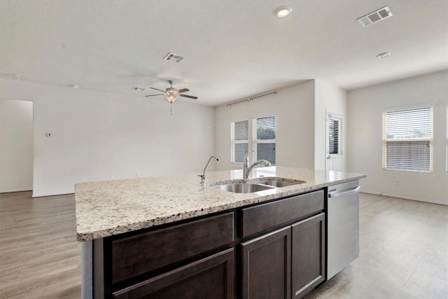 kitchen featuring a center island with sink, sink, stainless steel dishwasher, ceiling fan, and light stone countertops