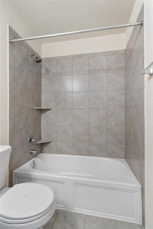 bathroom featuring tile patterned flooring, a textured ceiling, tiled shower / bath combo, and toilet