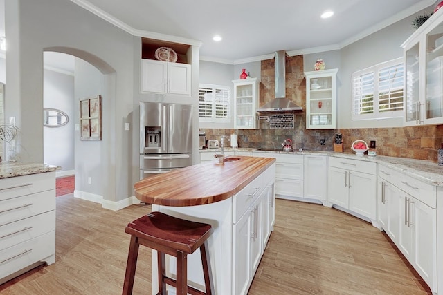 kitchen with stainless steel refrigerator with ice dispenser, white cabinetry, a kitchen island with sink, and wall chimney exhaust hood