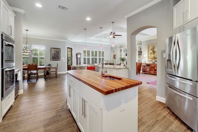 kitchen with decorative light fixtures, white cabinets, wooden counters, a center island with sink, and appliances with stainless steel finishes